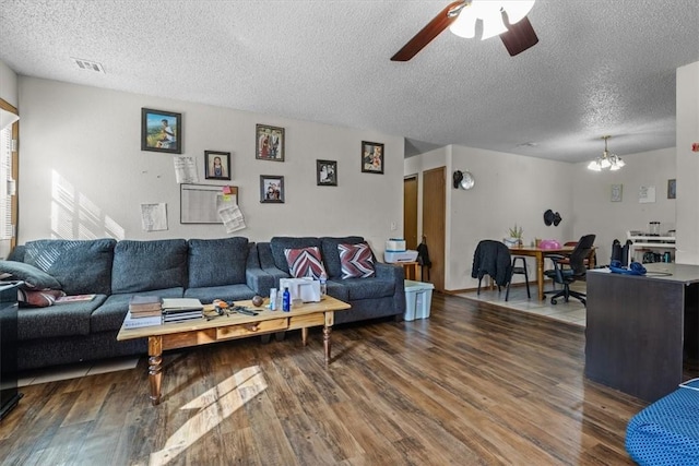 living area featuring wood finished floors, ceiling fan with notable chandelier, visible vents, and a textured ceiling