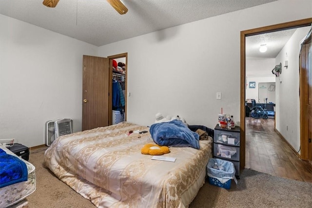 bedroom featuring a textured ceiling, a walk in closet, a ceiling fan, and wood finished floors