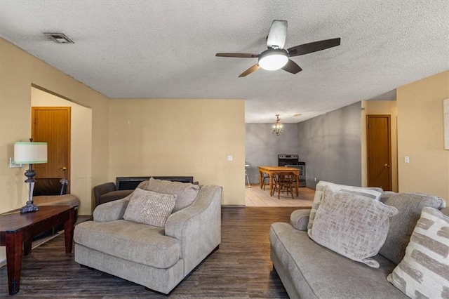 living area with dark wood-style floors, ceiling fan with notable chandelier, visible vents, and a textured ceiling