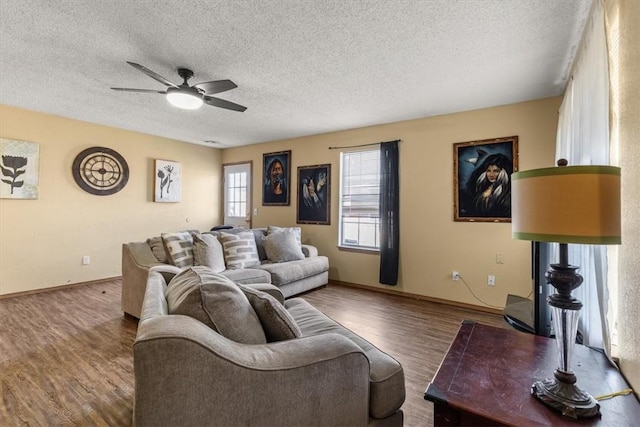 living area featuring baseboards, a textured ceiling, a ceiling fan, and wood finished floors