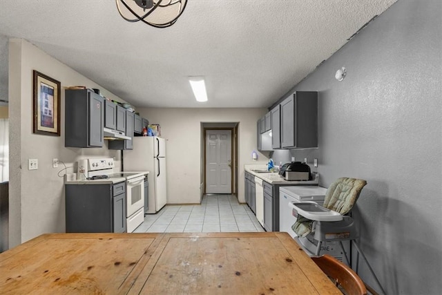 kitchen with white appliances, light tile patterned flooring, light countertops, under cabinet range hood, and a textured ceiling