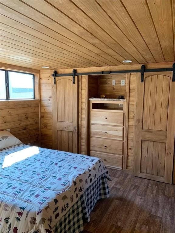 bedroom featuring a barn door, wooden walls, dark wood-style flooring, and wooden ceiling