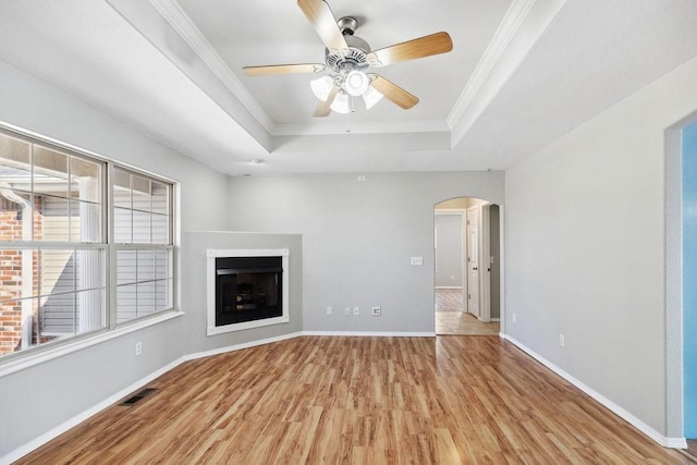 unfurnished living room with arched walkways, visible vents, crown molding, and a tray ceiling