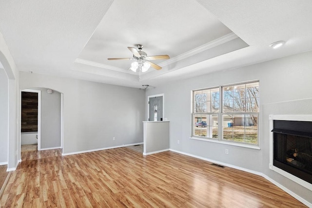 unfurnished living room with arched walkways, visible vents, light wood-type flooring, and a raised ceiling