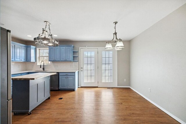 kitchen featuring blue cabinetry, butcher block counters, wood finished floors, a notable chandelier, and a sink