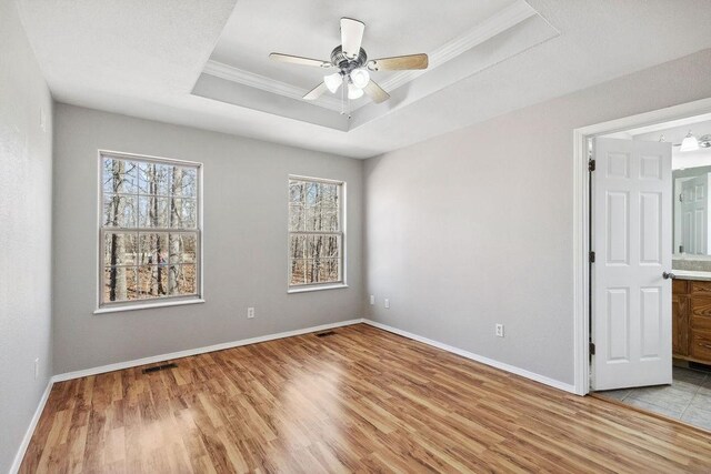 spare room featuring baseboards, visible vents, ceiling fan, a raised ceiling, and light wood-type flooring