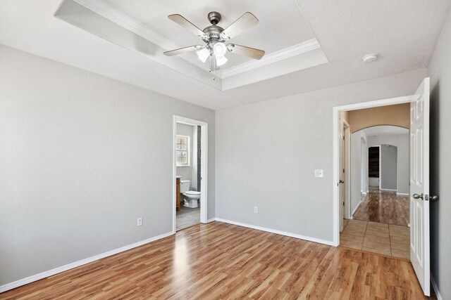 unfurnished bedroom with baseboards, arched walkways, crown molding, light wood-style floors, and a raised ceiling