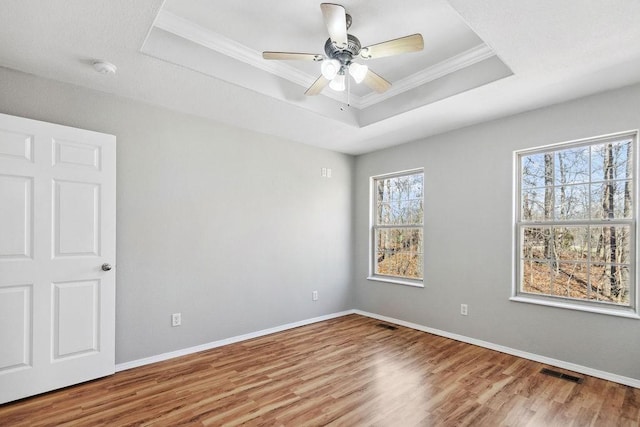 spare room with wood finished floors, visible vents, baseboards, crown molding, and a raised ceiling