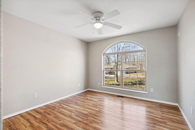 empty room featuring ceiling fan, visible vents, baseboards, and wood finished floors