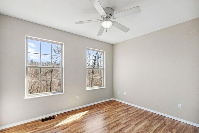 spare room with a ceiling fan, wood finished floors, visible vents, and baseboards