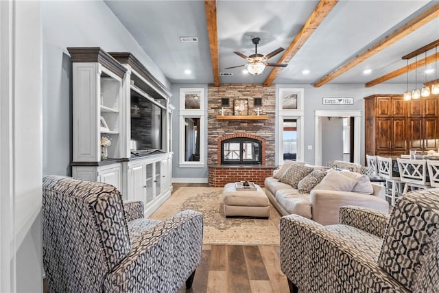 living room featuring visible vents, a large fireplace, ceiling fan, beamed ceiling, and dark wood-style flooring