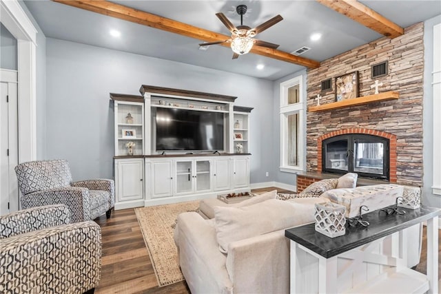 living area featuring beamed ceiling, visible vents, a fireplace, ceiling fan, and dark wood-style flooring