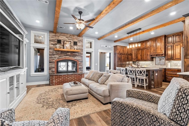 living area featuring visible vents, a large fireplace, ceiling fan, dark wood finished floors, and beam ceiling