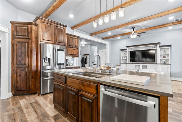 kitchen featuring ceiling fan, a center island with sink, light wood-style flooring, appliances with stainless steel finishes, and a sink