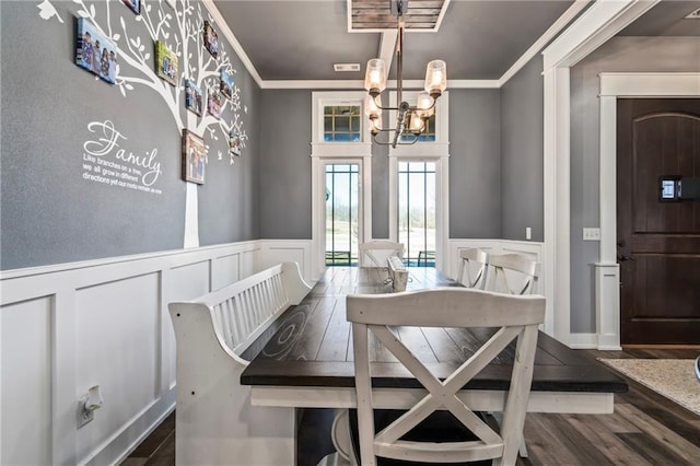 dining area with wood finished floors, an inviting chandelier, ornamental molding, and wainscoting