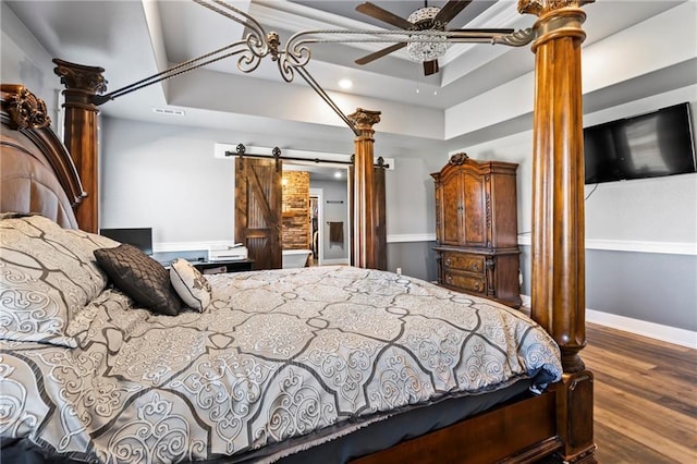 bedroom featuring visible vents, baseboards, a barn door, a tray ceiling, and wood finished floors