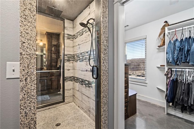 full bathroom with a walk in closet, baseboards, a stall shower, and concrete floors