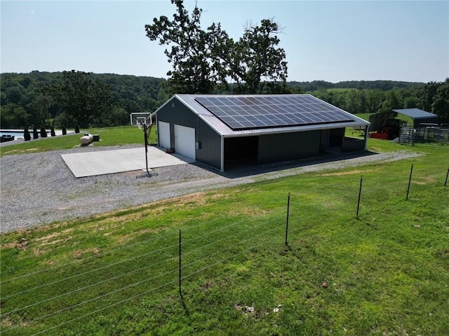 view of outbuilding featuring gravel driveway, an outbuilding, a wooded view, and solar panels