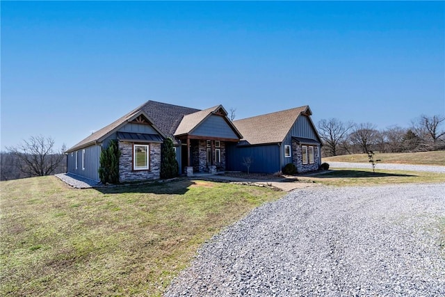 view of front of home with board and batten siding, a front lawn, stone siding, and driveway