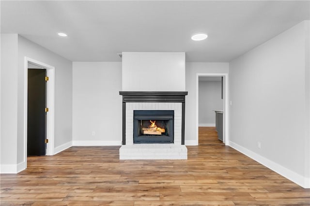 unfurnished living room featuring a brick fireplace, recessed lighting, wood finished floors, and baseboards