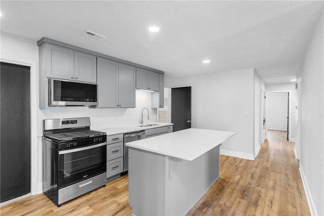 kitchen with light wood-style flooring, gray cabinets, a sink, light countertops, and appliances with stainless steel finishes