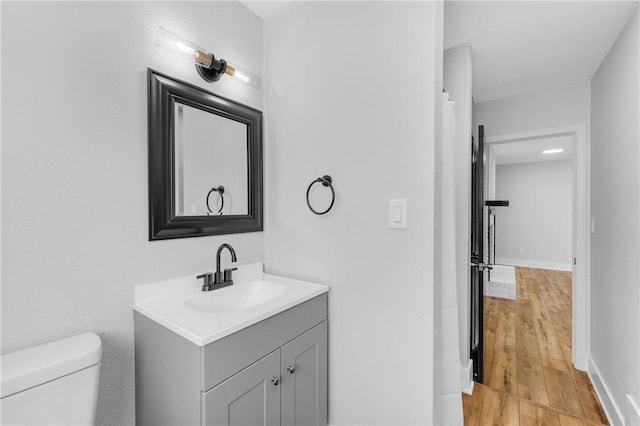 bathroom with baseboards, toilet, wood finished floors, and vanity