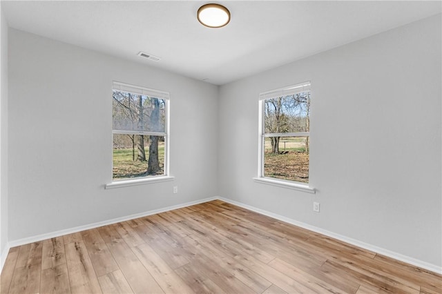 empty room with wood finished floors, visible vents, and baseboards