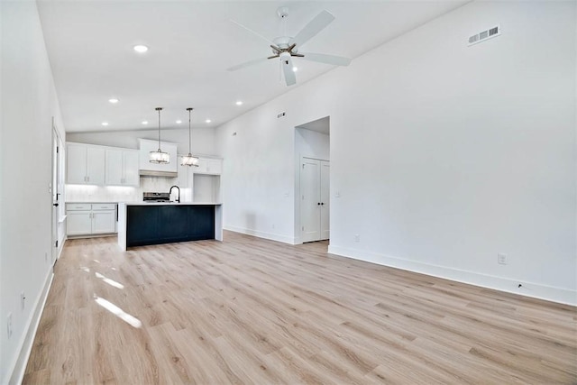 unfurnished living room with light wood-type flooring, visible vents, a ceiling fan, a sink, and baseboards