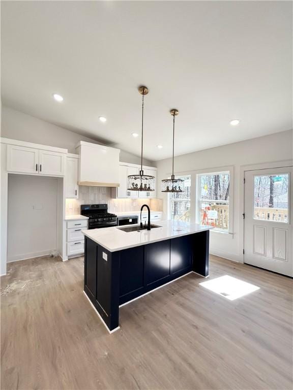 kitchen featuring a center island with sink, a sink, decorative backsplash, black gas range, and white cabinetry