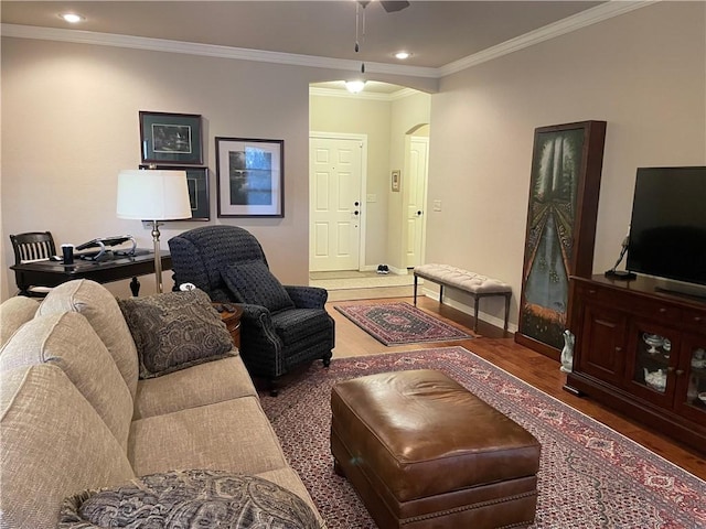 living area featuring ornamental molding, wood finished floors, arched walkways, baseboards, and ceiling fan