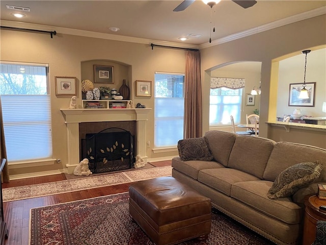 living area with visible vents, ornamental molding, a ceiling fan, wood finished floors, and arched walkways