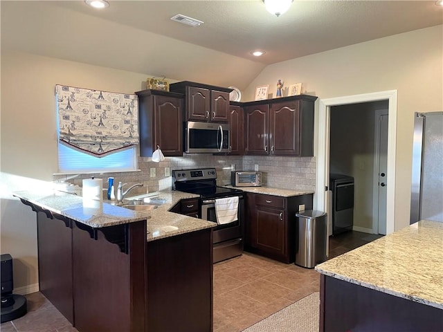 kitchen featuring dark brown cabinets, decorative backsplash, appliances with stainless steel finishes, a peninsula, and a sink