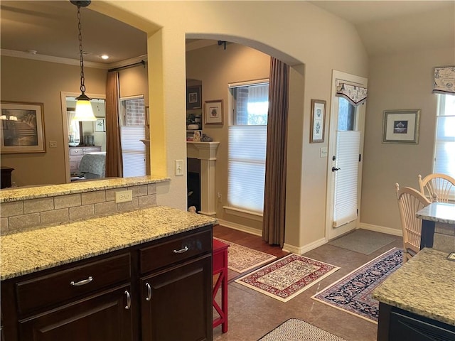 kitchen with light stone countertops, baseboards, lofted ceiling, arched walkways, and dark brown cabinets