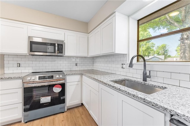 kitchen featuring white cabinets, stainless steel appliances, light wood-style flooring, and a sink