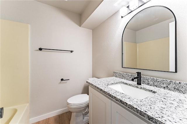 bathroom with toilet, vanity, baseboards, and wood finished floors