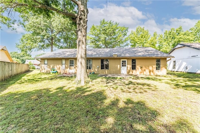 rear view of property featuring a lawn and fence