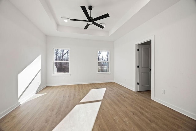 spare room featuring visible vents, ceiling fan, baseboards, wood finished floors, and a raised ceiling