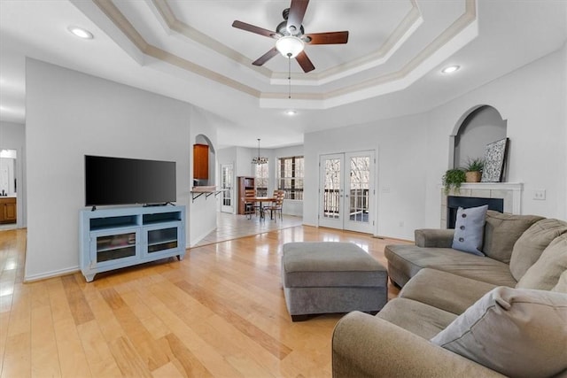 living room with baseboards, a tray ceiling, light wood-style flooring, arched walkways, and a ceiling fan