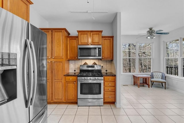 kitchen with tasteful backsplash, light tile patterned floors, brown cabinets, appliances with stainless steel finishes, and a ceiling fan