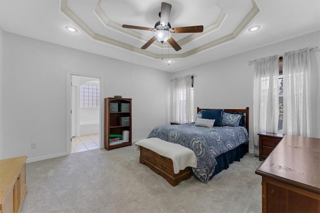 bedroom with light carpet, ensuite bathroom, a tray ceiling, recessed lighting, and ceiling fan