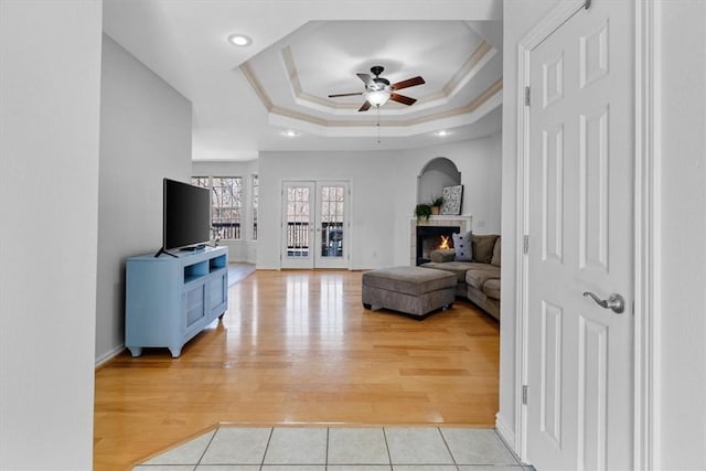 living area featuring a tray ceiling, a ceiling fan, light wood-style floors, and ornamental molding