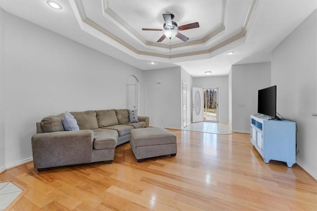 living room with baseboards, ornamental molding, light wood-style floors, a raised ceiling, and a ceiling fan