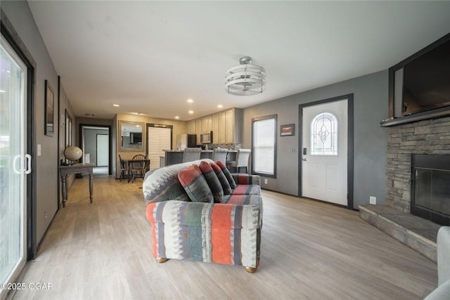 living room with a stone fireplace, recessed lighting, and light wood-style floors