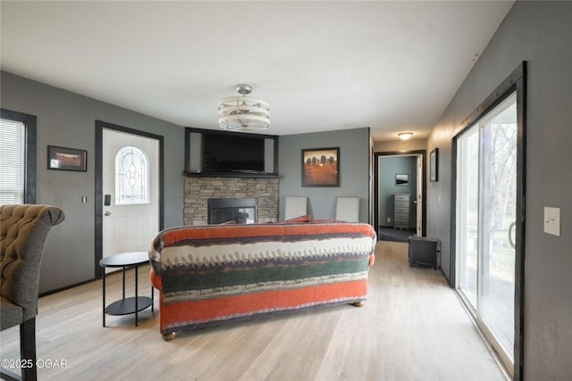 bedroom featuring a stone fireplace, multiple windows, and light wood-style floors