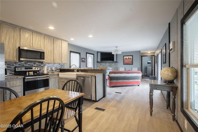 kitchen featuring visible vents, light wood-style flooring, stainless steel appliances, a peninsula, and decorative backsplash