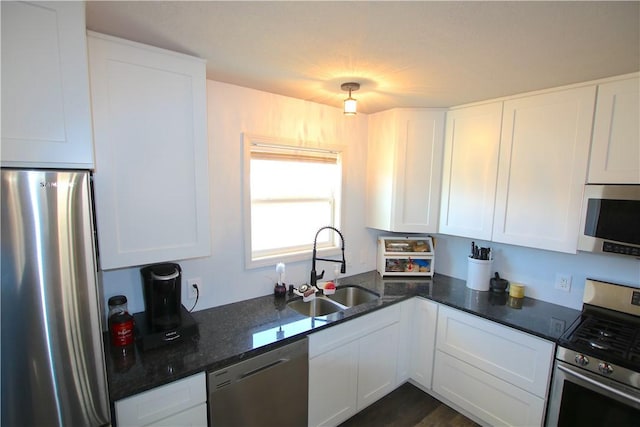 kitchen with white cabinets, stainless steel appliances, dark stone counters, and a sink