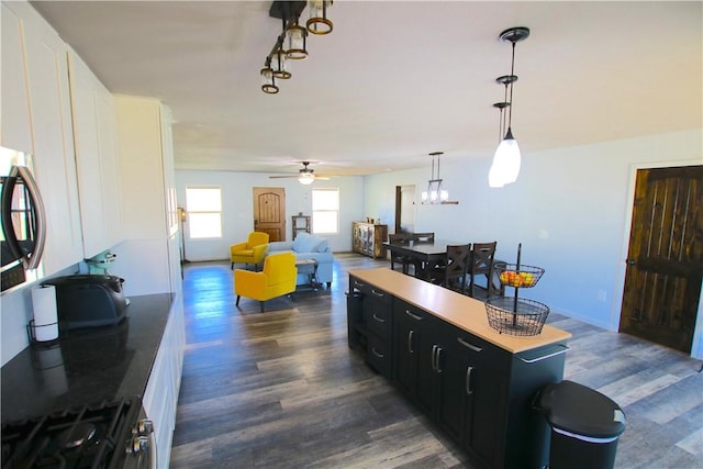 kitchen featuring stainless steel range with gas stovetop, dark cabinets, dark wood-style flooring, and ceiling fan with notable chandelier