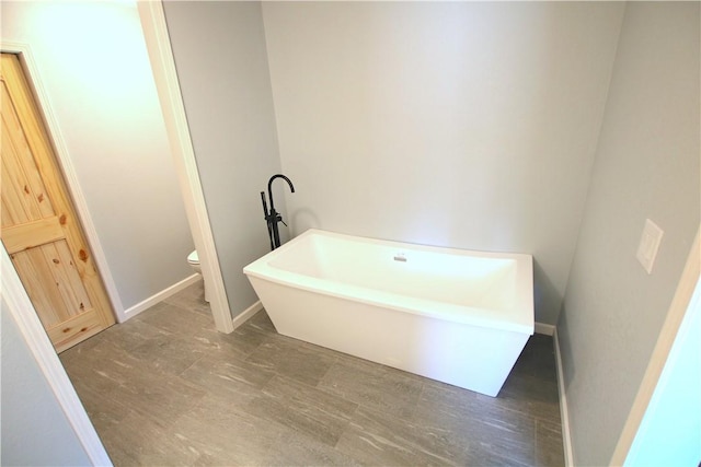 full bath featuring a freestanding bath, toilet, and baseboards