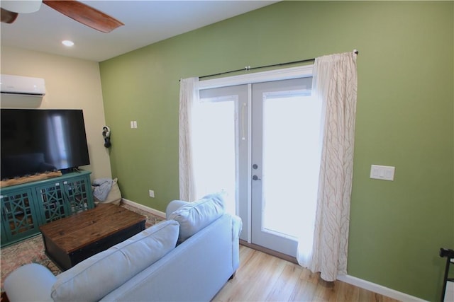 living area with baseboards, an AC wall unit, french doors, wood finished floors, and a ceiling fan