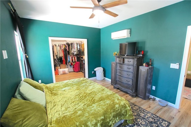 bedroom with a closet, an AC wall unit, baseboards, light wood-style floors, and a walk in closet